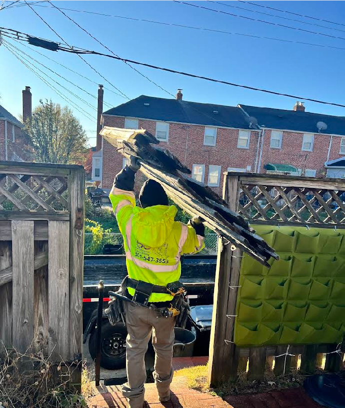 Worker in safety vest carrying roofing material near power lines and row houses.