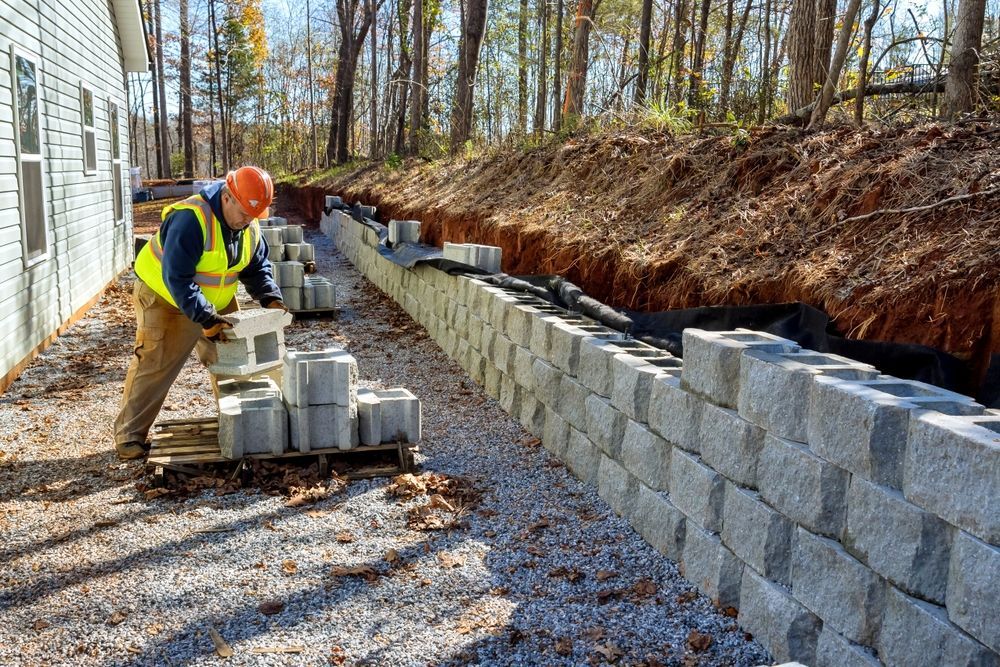 Construction worker building a retaining wall with concrete blocks next to a building.