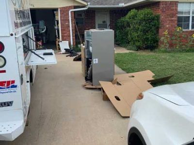 A refrigerator is sitting on top of a cardboard box in a driveway next to a truck.