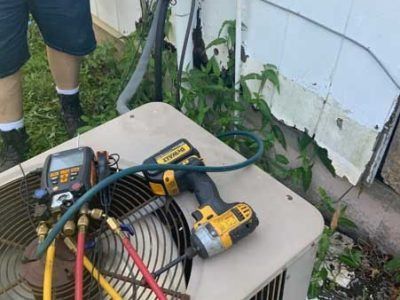 A man is working on an air conditioner outside of a house.