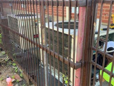 A man is working on an air conditioner behind a fence.