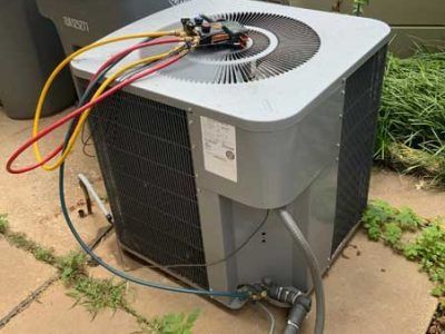 A large air conditioner is sitting on a sidewalk next to a trash can.