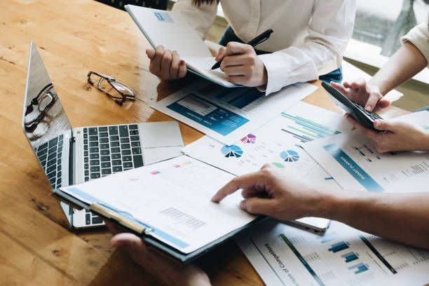 A group of people are sitting at a table looking at papers and a laptop.