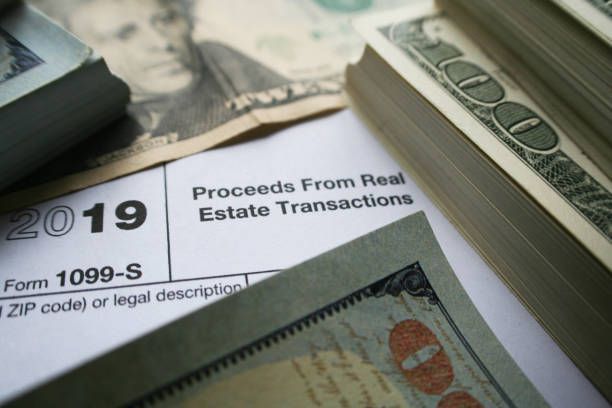 A stack of money sits on top of a form 1099-s