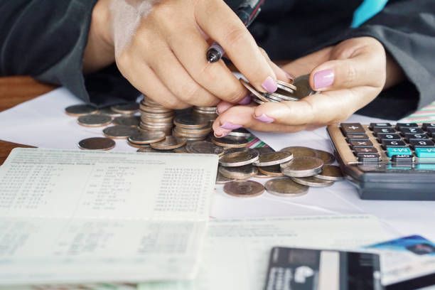 A woman is counting coins on a table with a calculator.