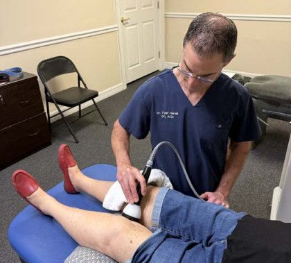 Doctor administering knee treatment with a device; patient lies on a table.
