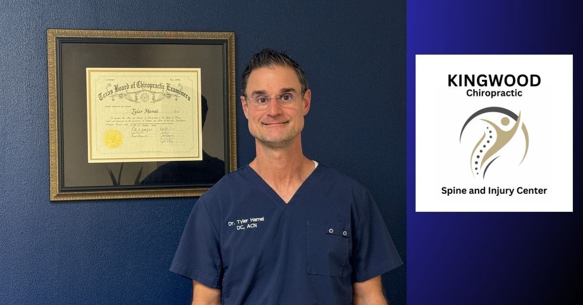 Man in scrubs stands in front of a framed certificate and Kingwood Chiropractic logo.