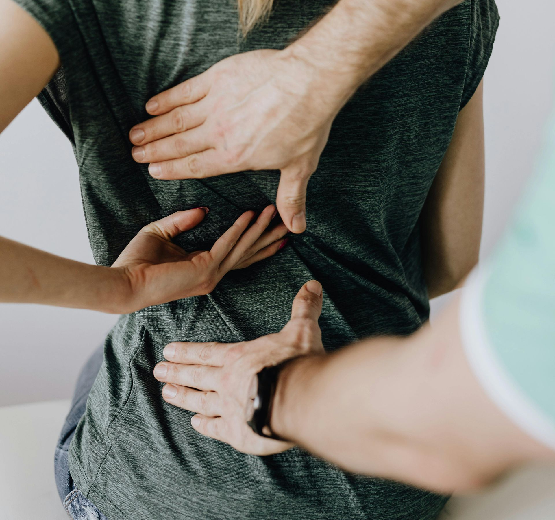 Hands of two people examining a person's lower back, likely for pain.