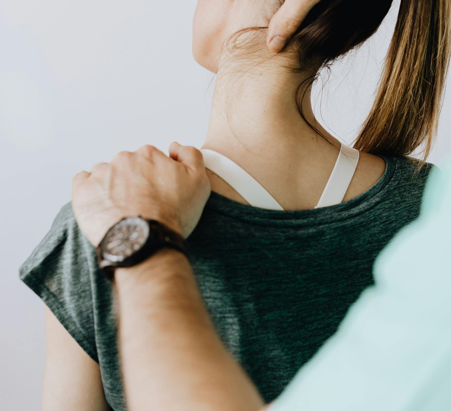 Person's neck and shoulder being examined. A hand touches the back of the neck, another on the shoulder.