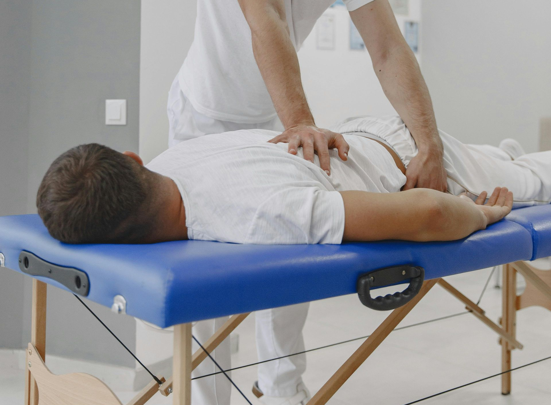 Person receiving abdominal massage on a blue massage table in a white-walled room.