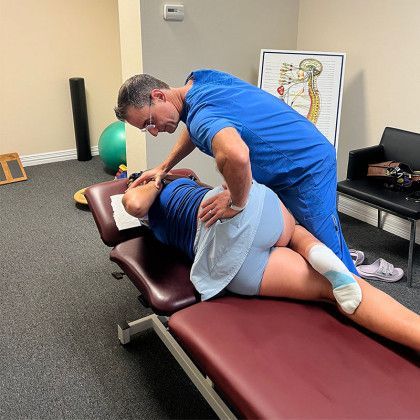 Doctor adjusting patient's back on exam table. Room with exercise equipment and poster.