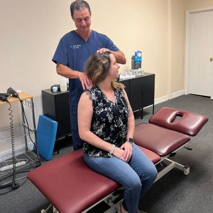 Chiropractor adjusting patient's neck in office. Patient sits on an examination table, the doctor uses his hands on patient's head.