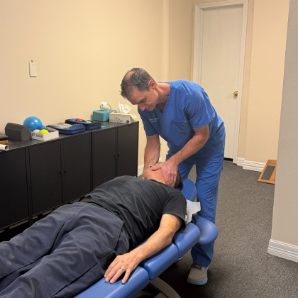 A healthcare provider in blue scrubs adjusts a person's head while they lie on an examination table.