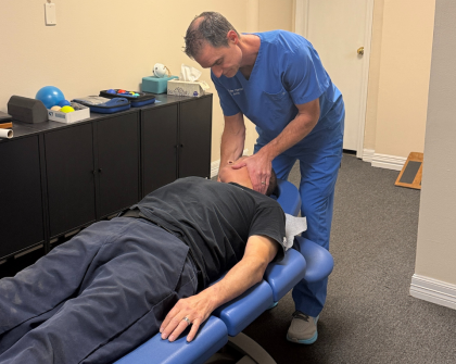 A healthcare provider in blue scrubs examines a patient's neck while he lies on a treatment table.