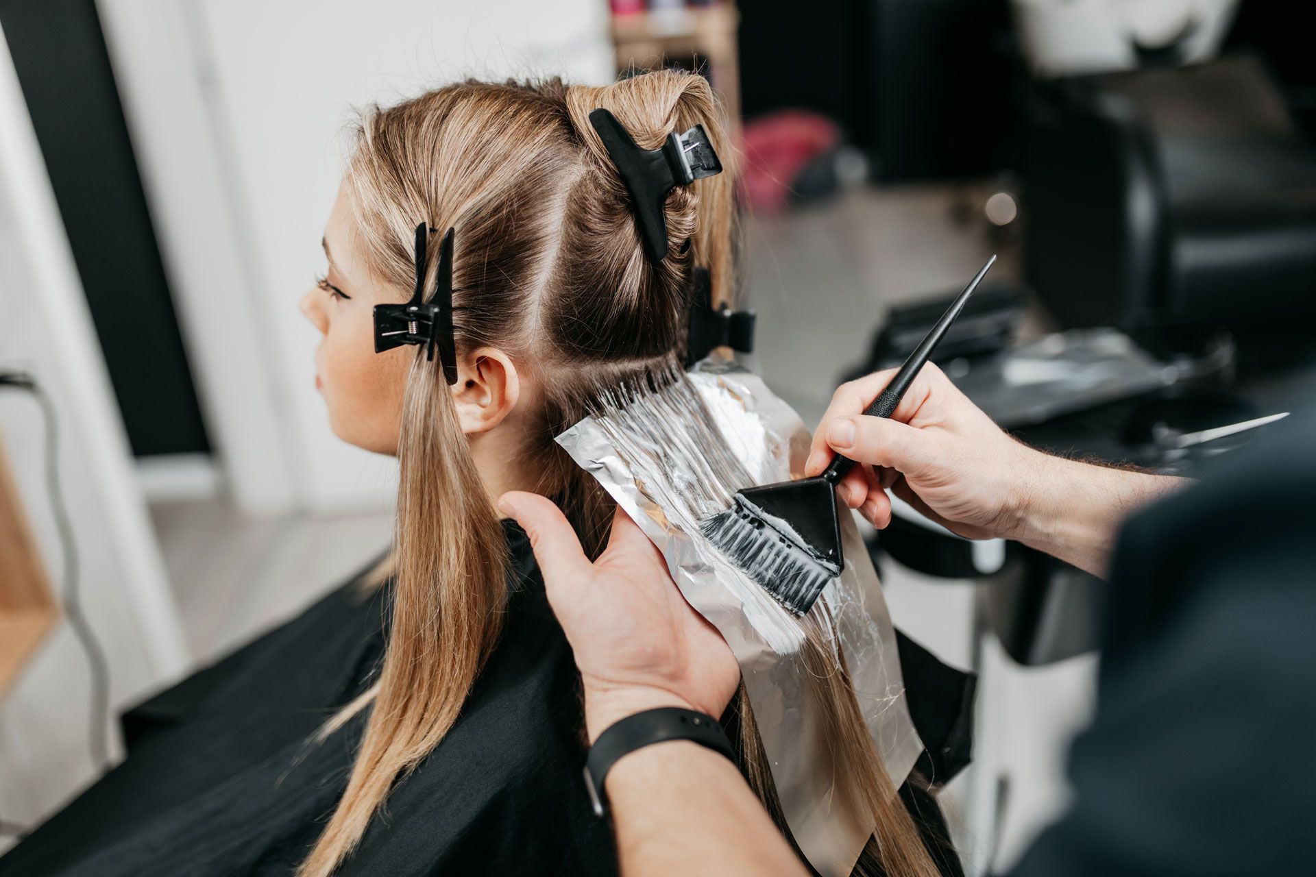 Hairdresser applying dye to a client's hair with a brush and foil in a salon.