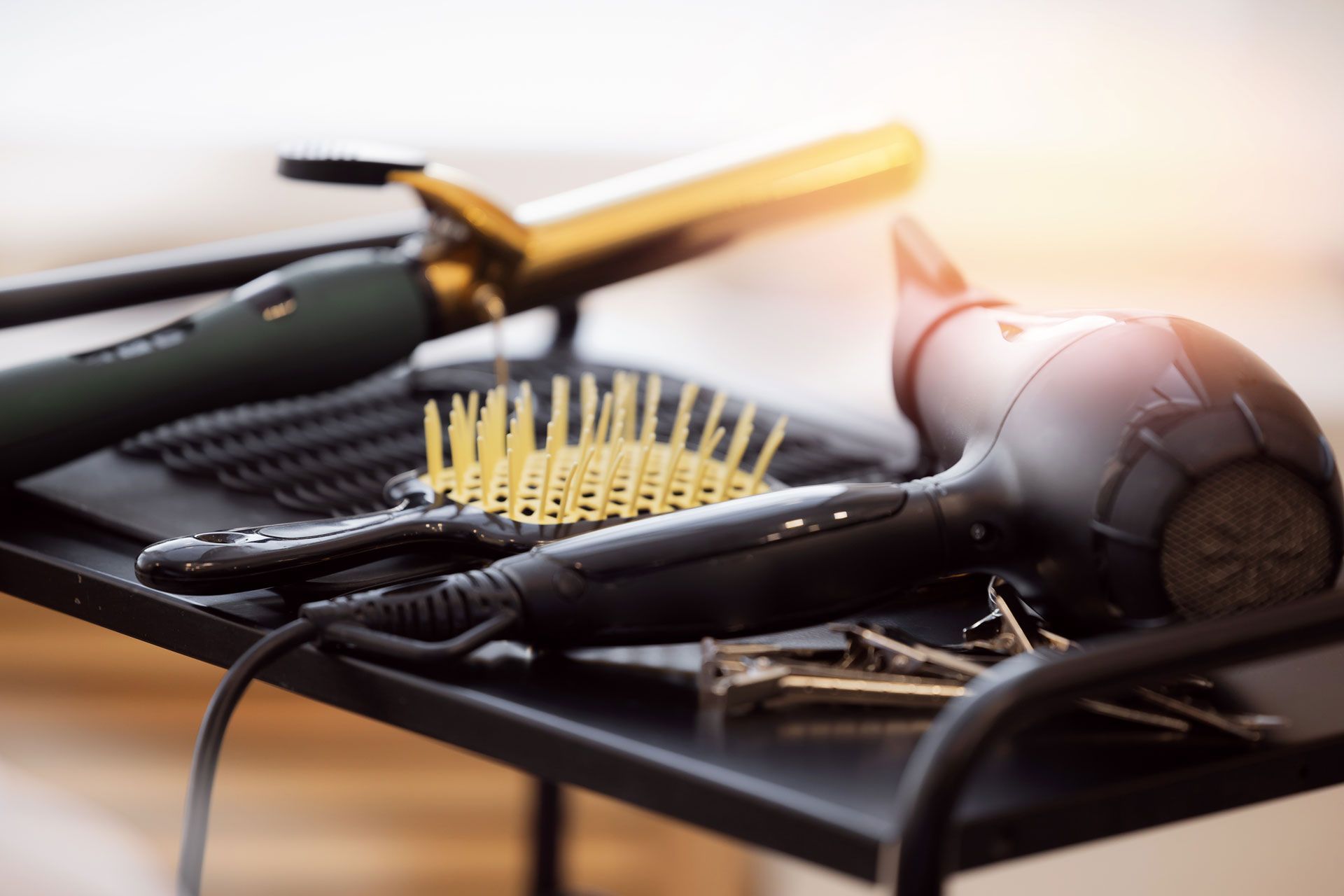 Hair styling tools on a black tray: curling iron, brush, hair dryer, and clips.