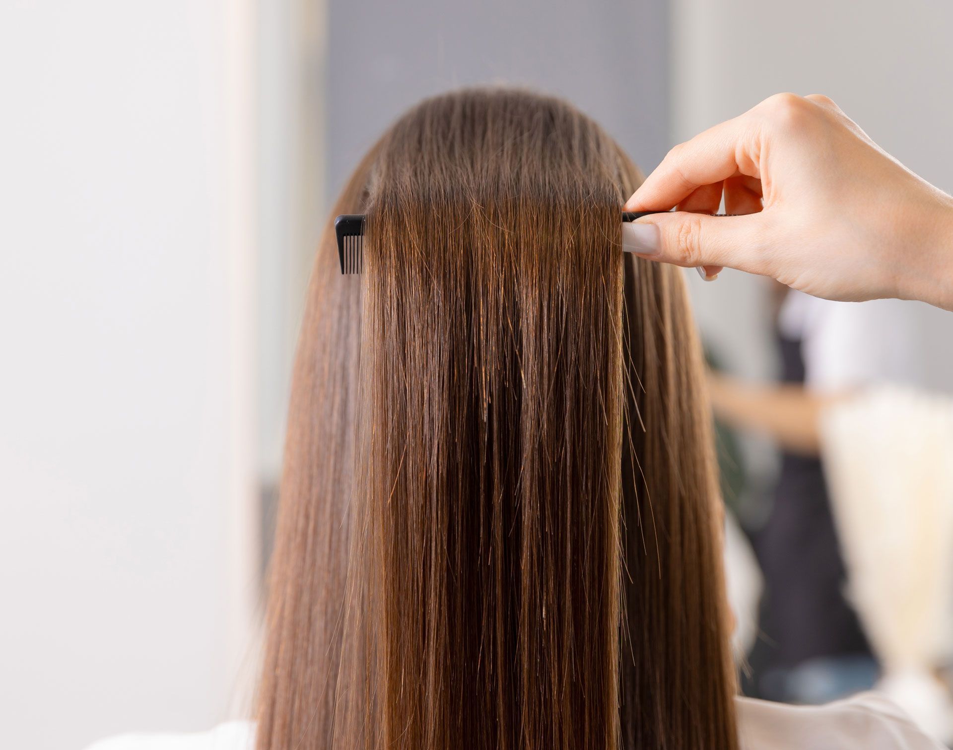 Person's straight brown hair being styled by a hand holding a small black hair accessory.