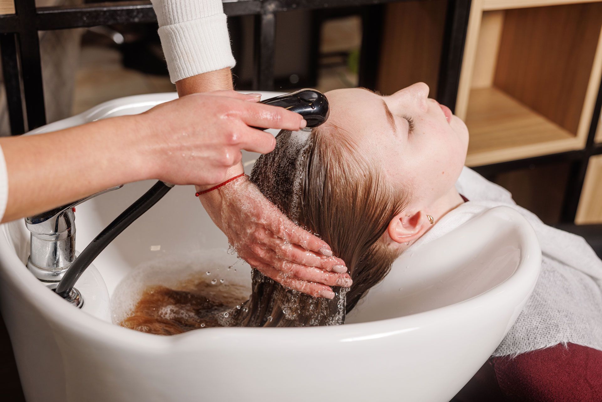 Woman getting hair washed in a salon basin, stylist's hands washing hair with a shower head.
