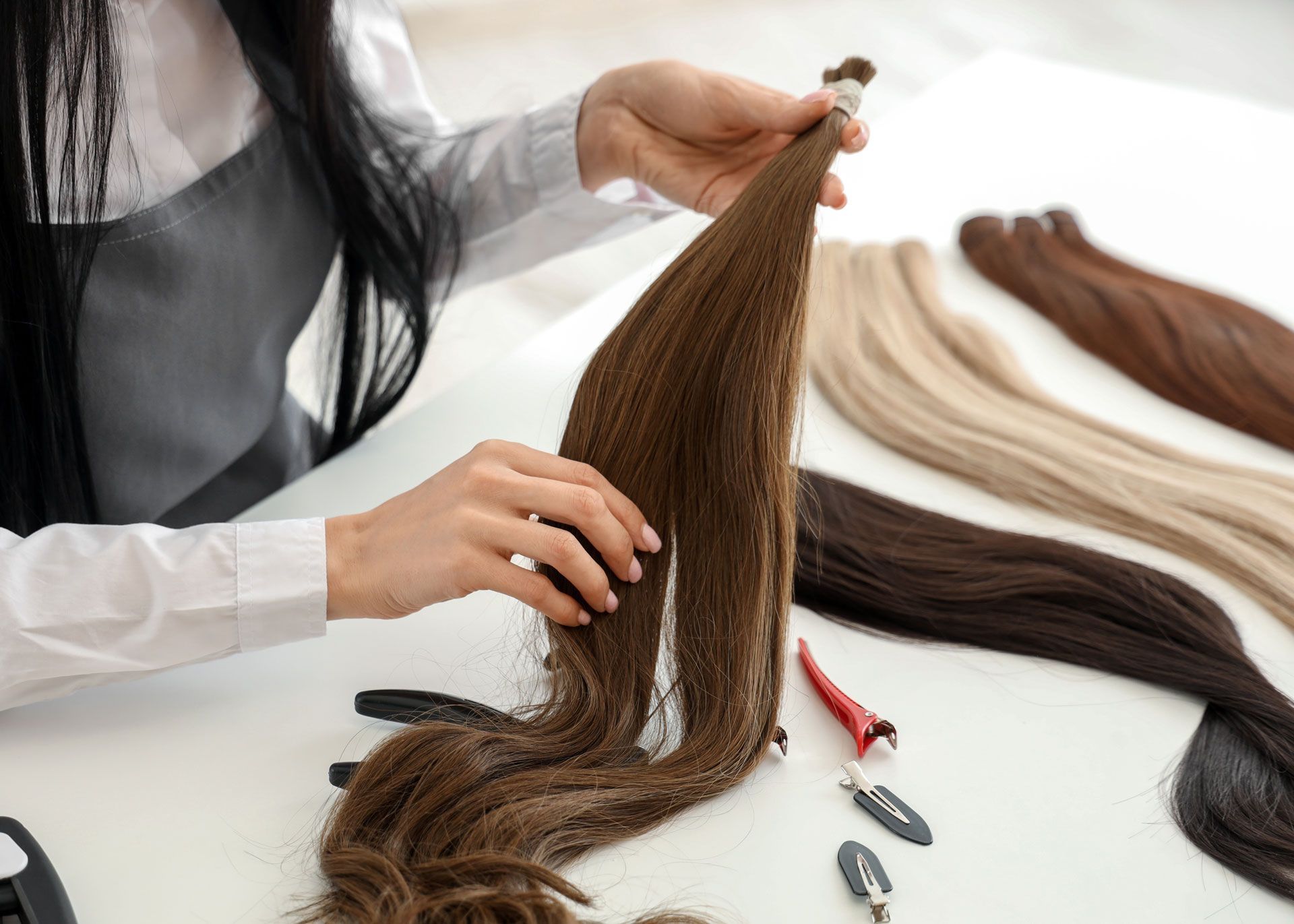 Person holding brown hair extensions, comparing them with other shades on a table.