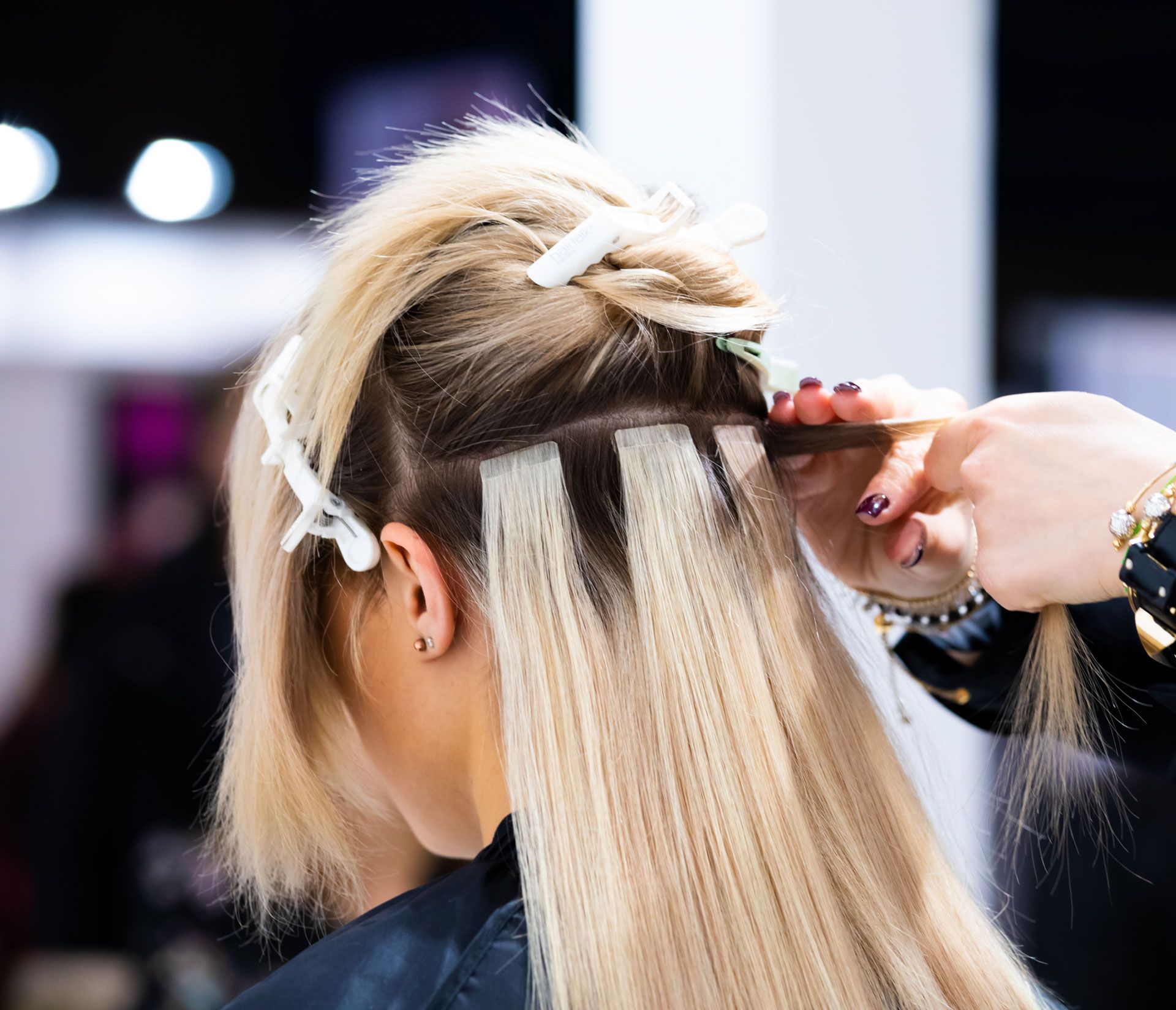 Hair stylist applying tape-in hair extensions to a client's light blonde hair.