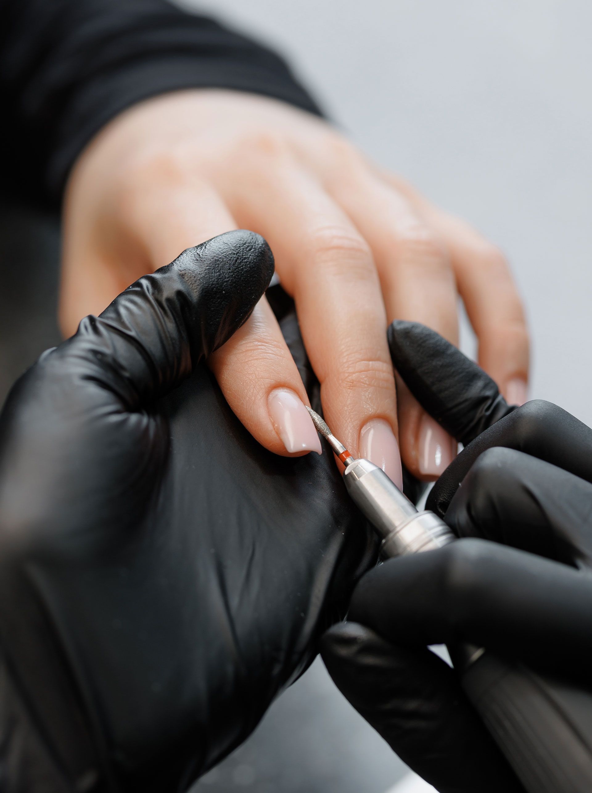 Manicurist using a small tool to apply nail polish to a person's finger, hands gloved.