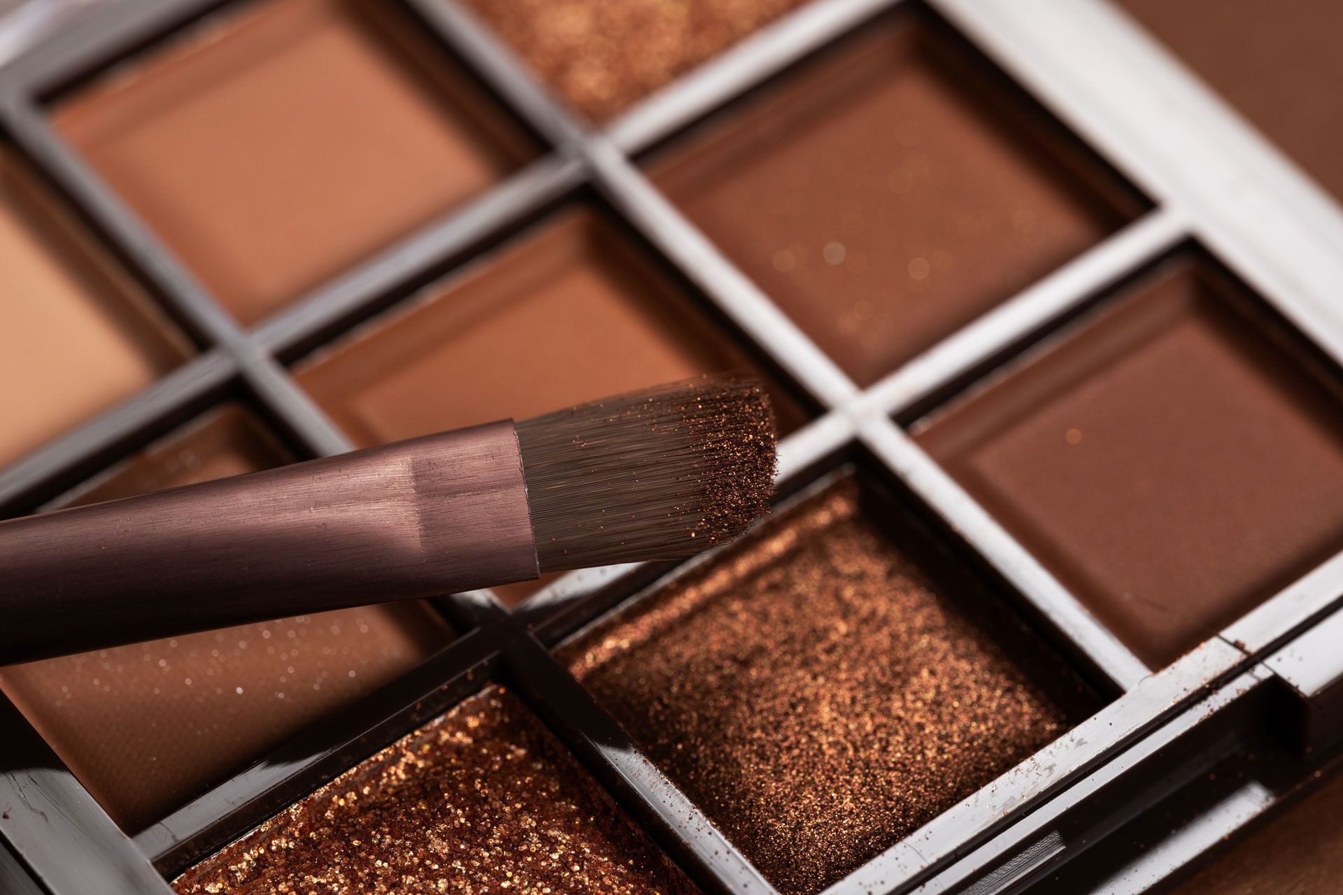 Eyeshadow palette with brown shades, angled brush resting on palette.