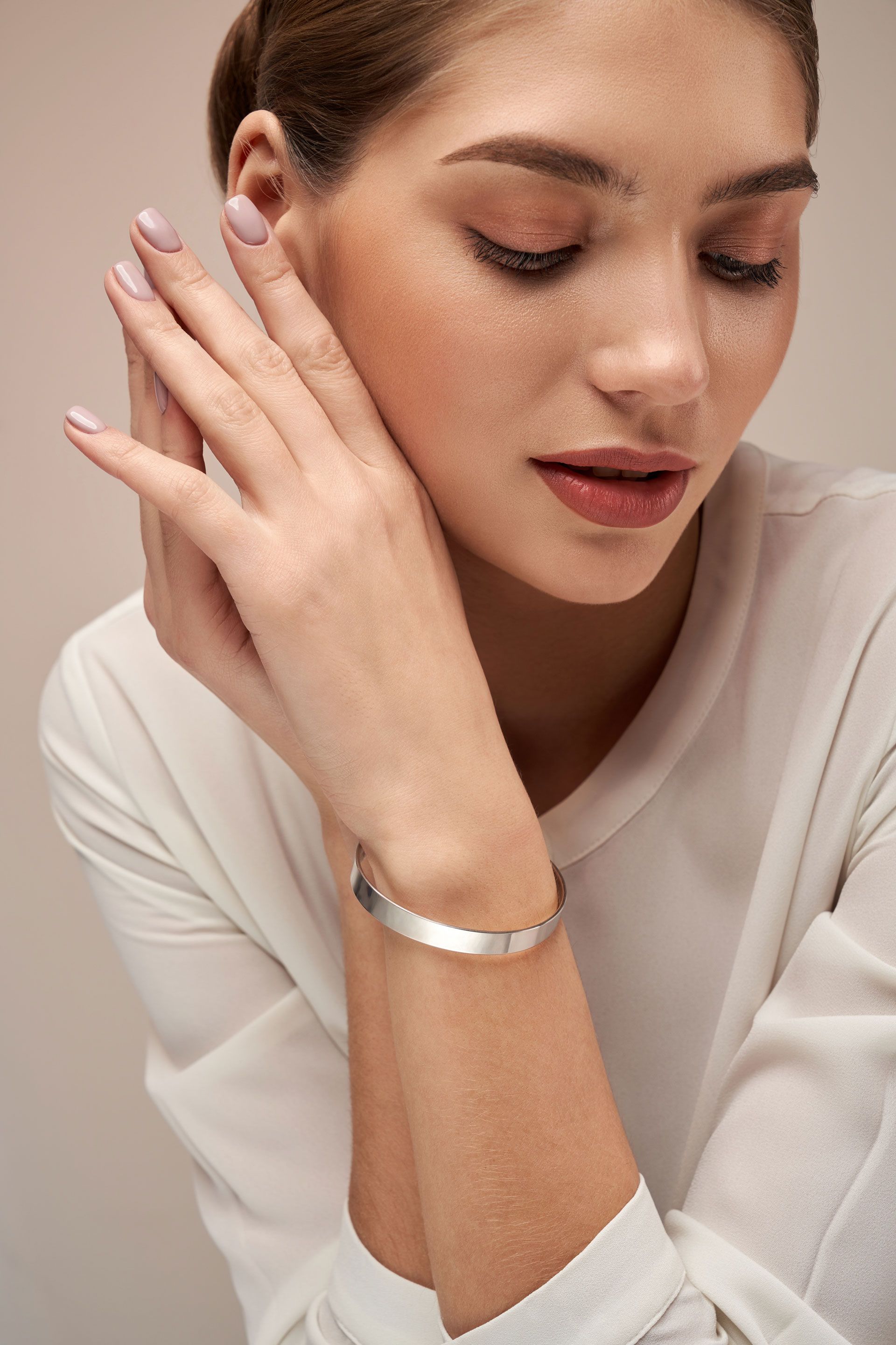 Woman with pale skin wearing a silver bracelet, resting her hands near her face.