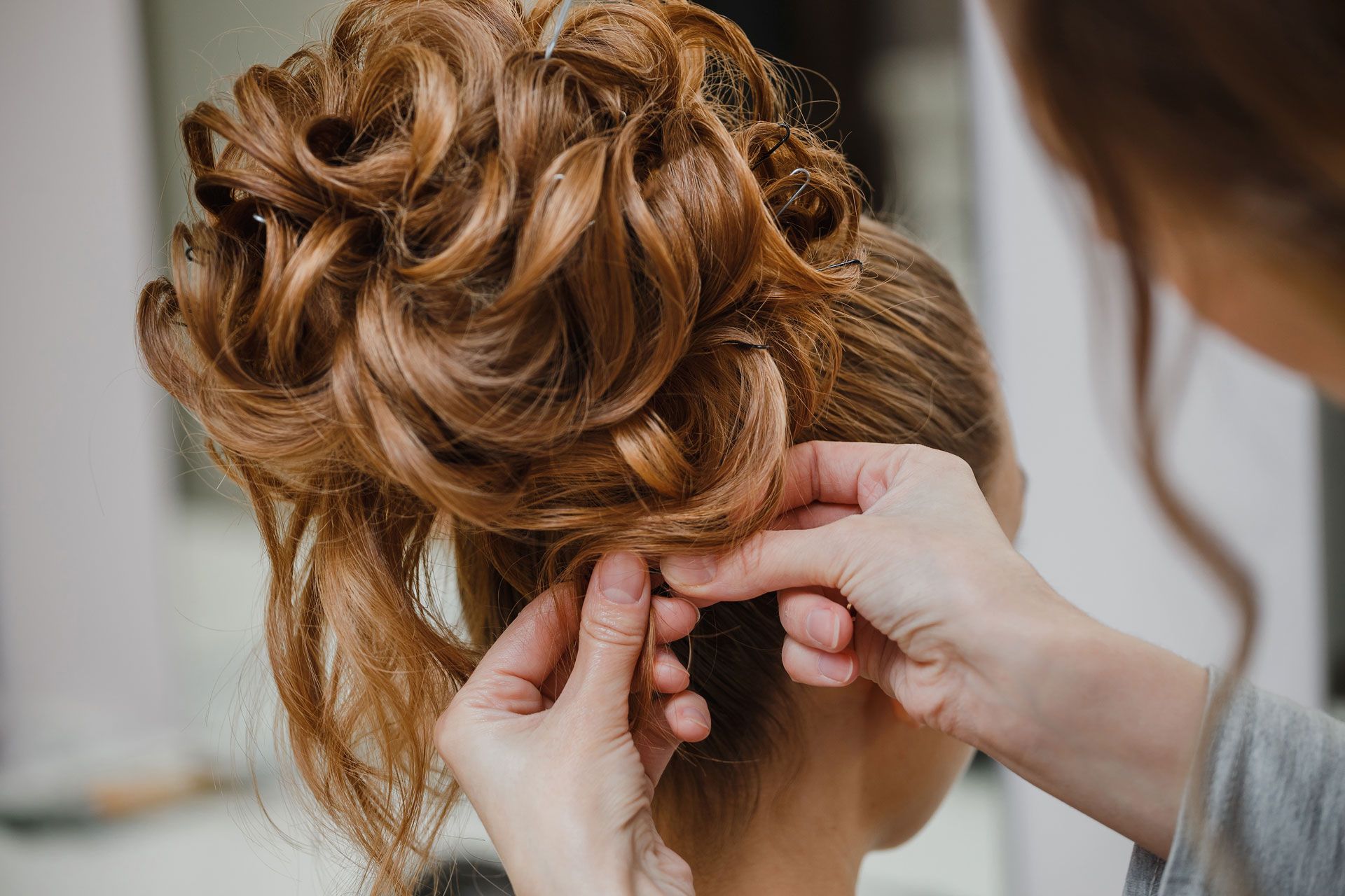 Hands styling a woman's brown hair into an updo, in a salon setting.