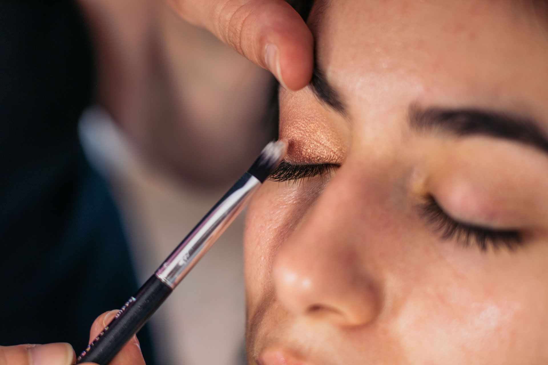 Makeup artist applying eyeshadow to a person's closed eye with a brush.