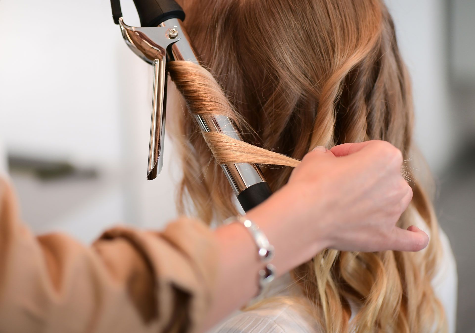 Woman's hair being curled with a curling iron by another person's hand.