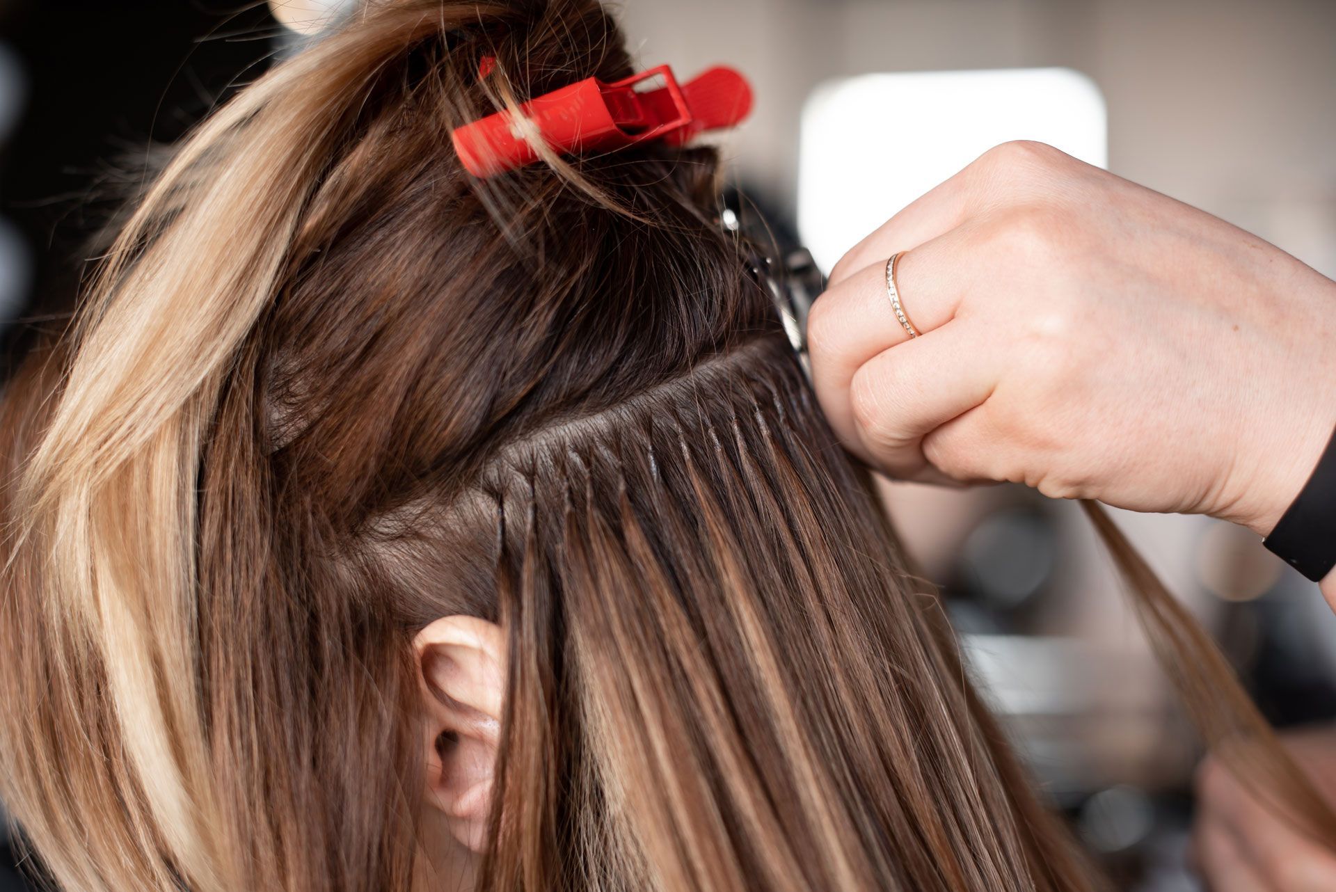 Hair extensions being applied; a person's hand holds strands while another hand works on the attachment.