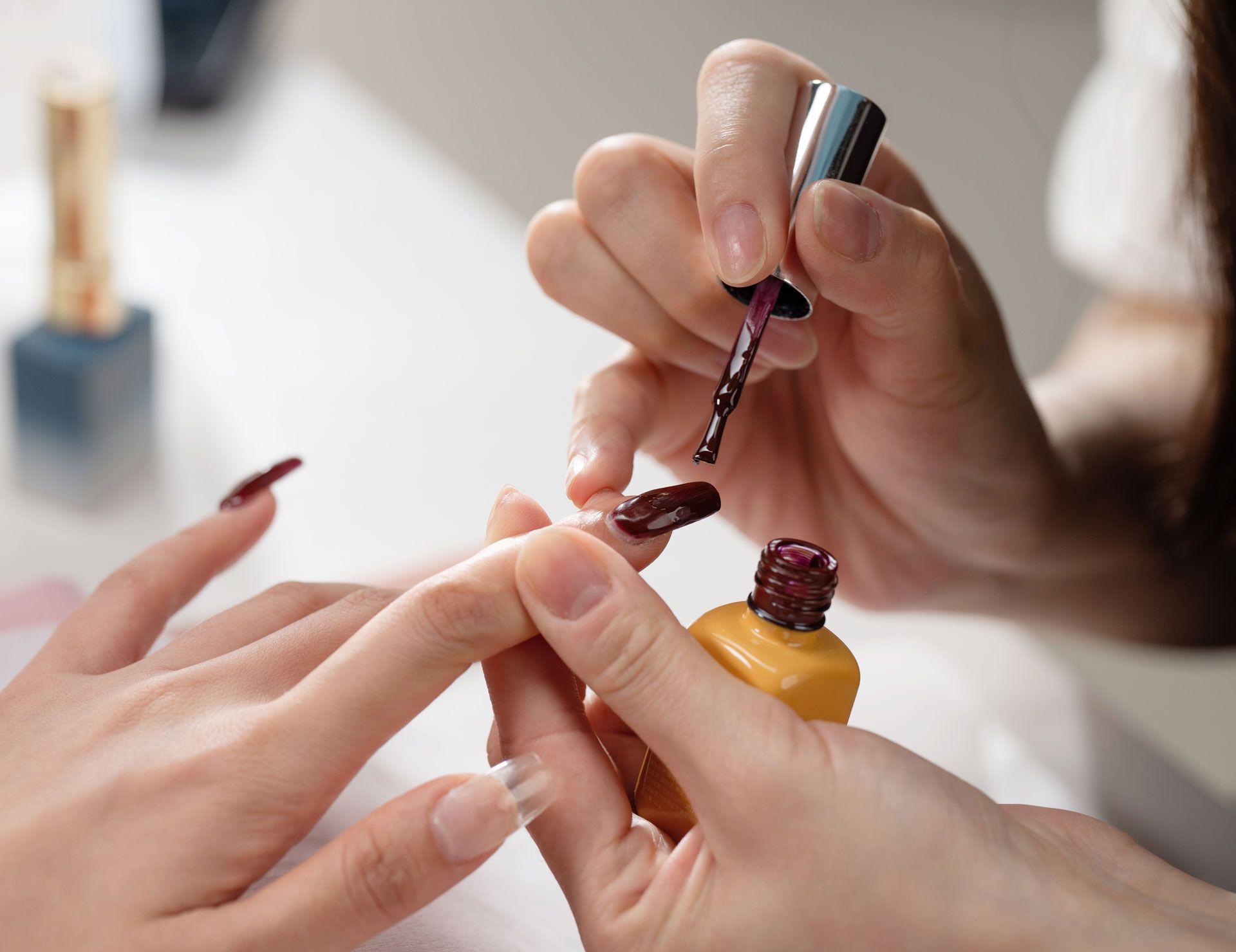 Person applying dark red nail polish to another person's nails.