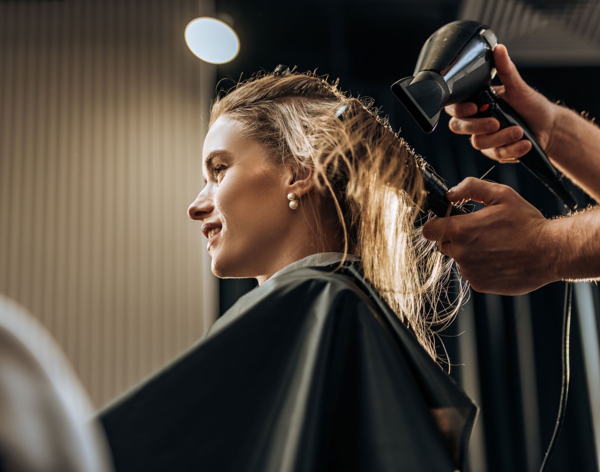 Woman getting her hair blow-dried at a salon, smiling.