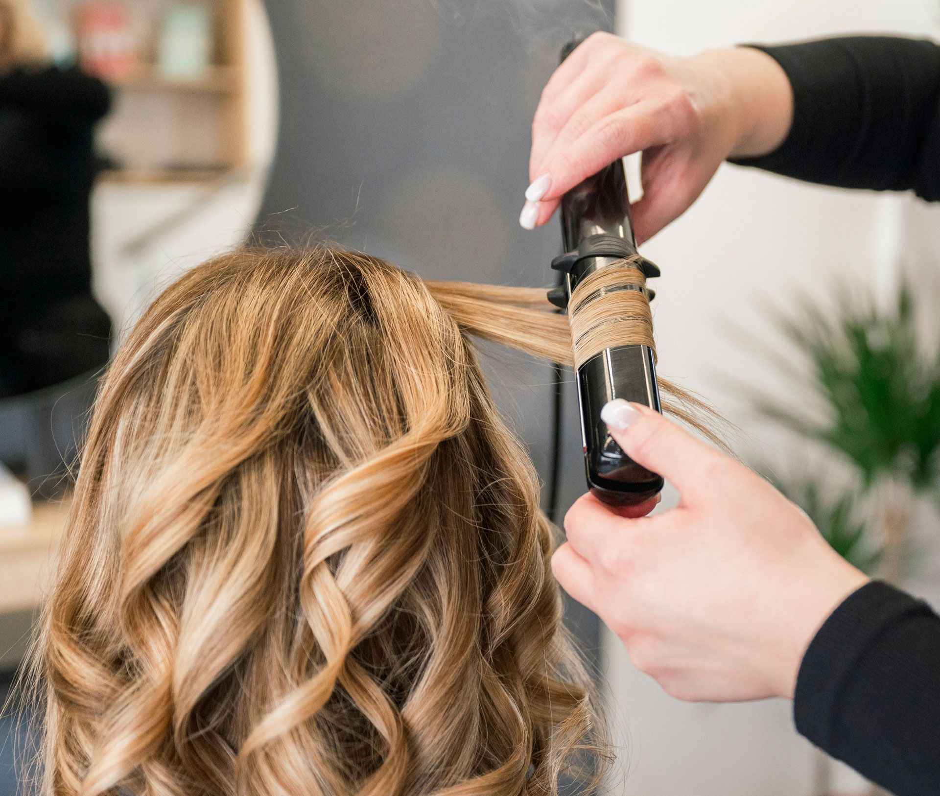 Hair stylist curling blonde hair with a curling iron in a salon.