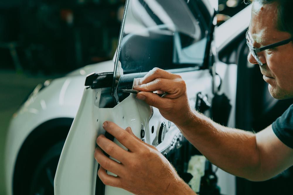 A man is working on a car door with a screwdriver.