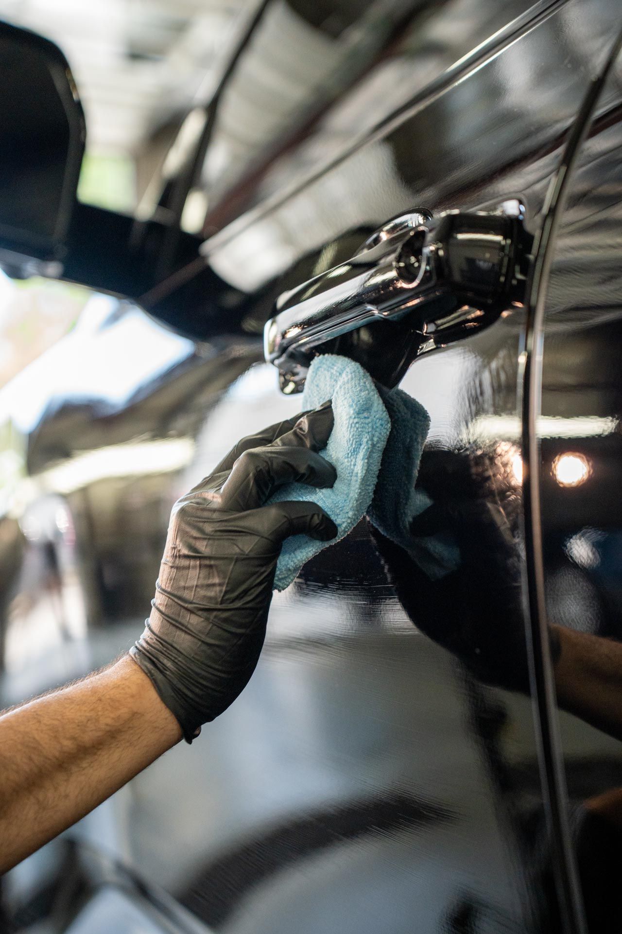 Ceramic Coating - A person wearing black gloves is cleaning a car with a blue cloth