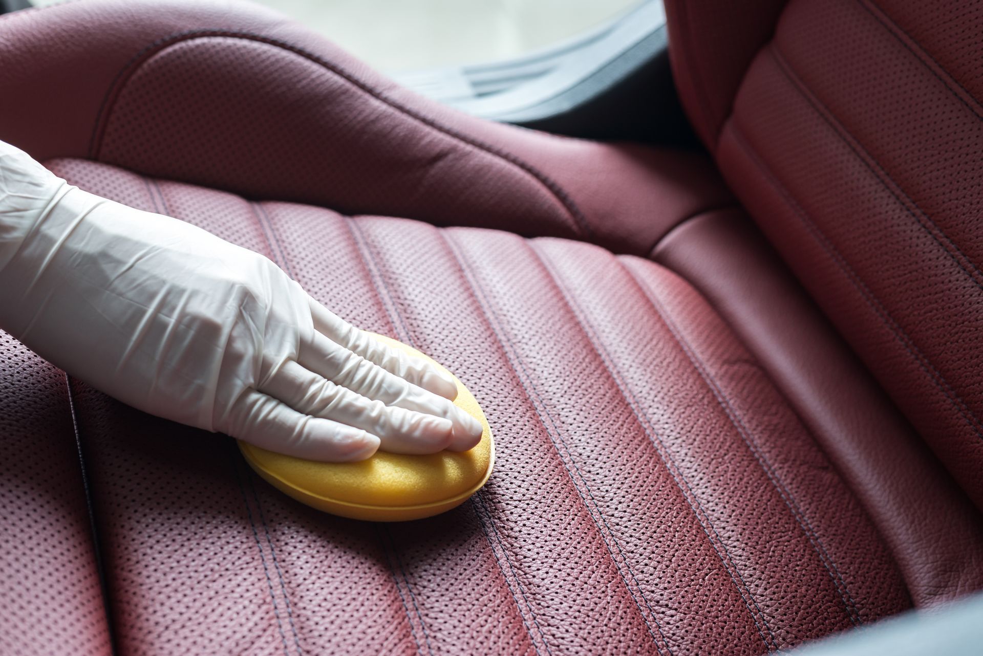 Interior Coating - A person wearing gloves is cleaning a red leather seat with a yellow sponge