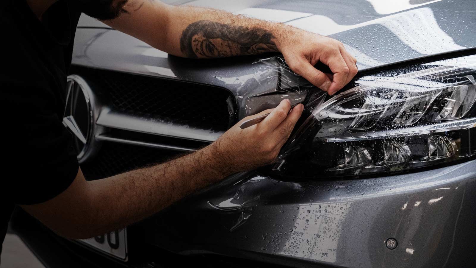 A man is applying a protective film to the headlights of a mercedes benz.