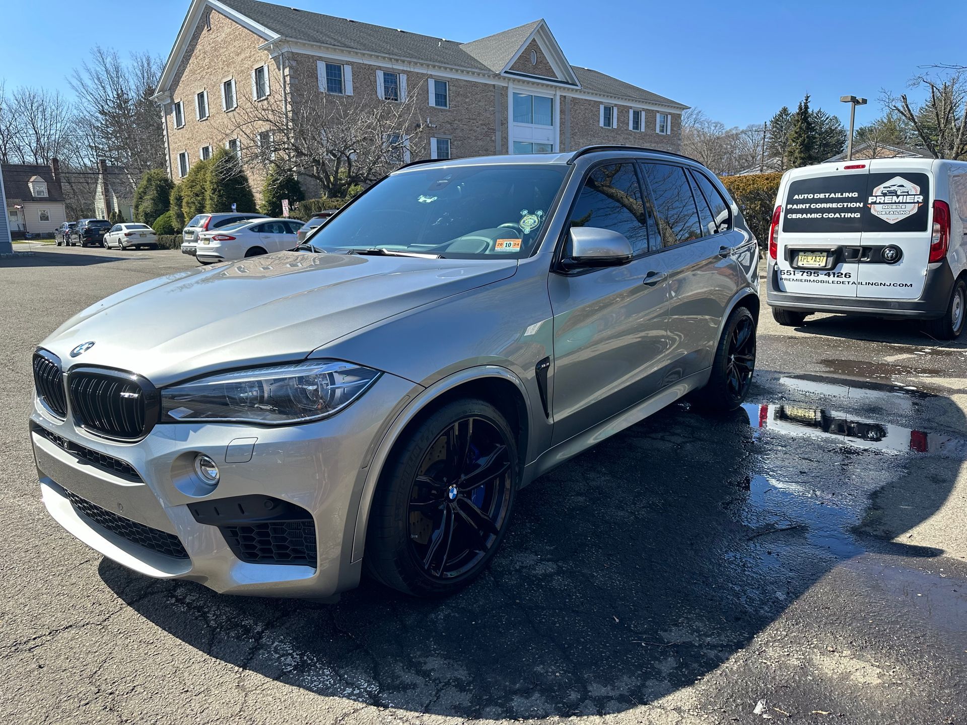a silver bmw x5 m is parked in a parking lot in front of a building .