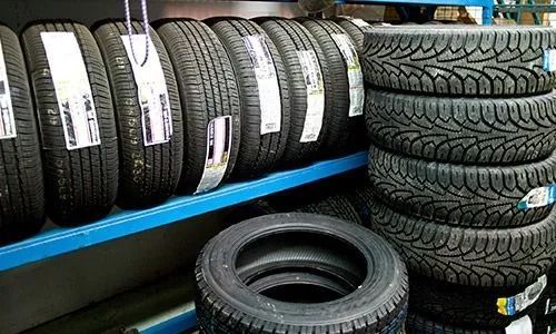 Montones de neumáticos negros para coches en estanterías metálicas azules en una tienda de neumáticos.
