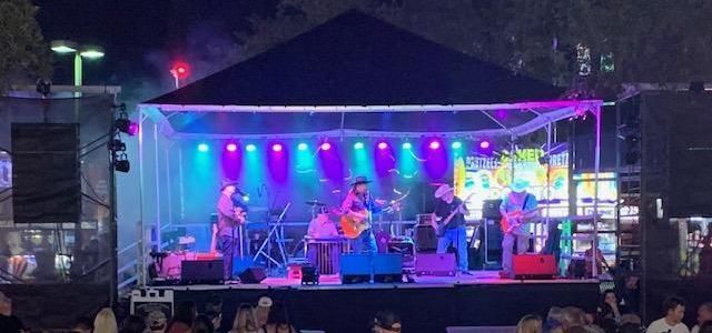 A black and white photo of a man playing a guitar on a stage.