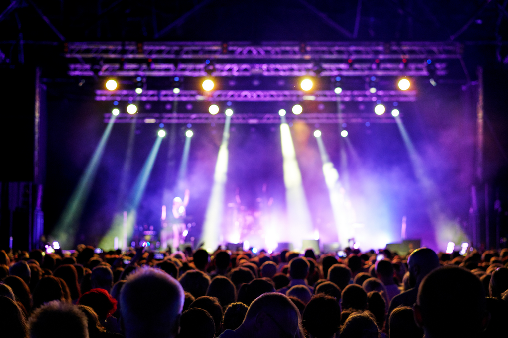 A crowd of people are sitting in front of a stage at a concert.