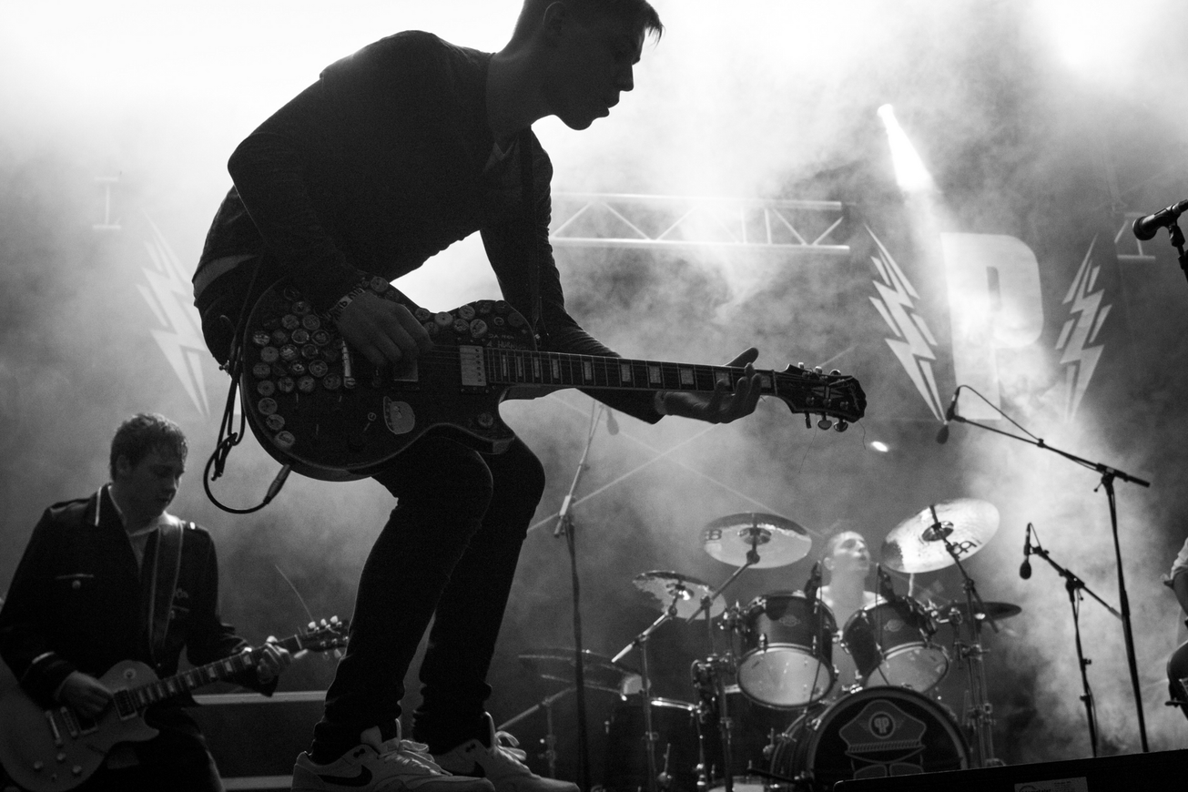 A black and white photo of a man playing a guitar on a stage.