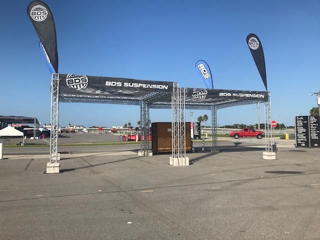 A red truck is parked in a parking lot under a canopy that says bob suspension