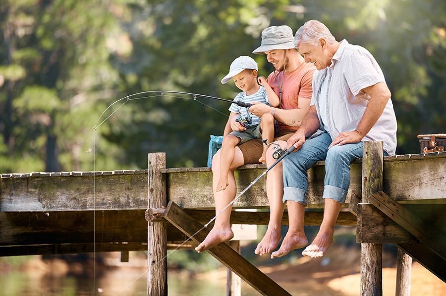 Three people fishing on a wooden dock: a child, an adult, and an older person. The boy holds the rod.