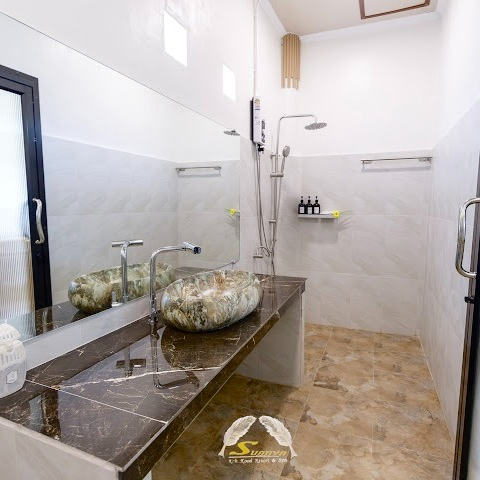 Bathroom with marble sink and countertop, shower, mirror, and beige tile floor.