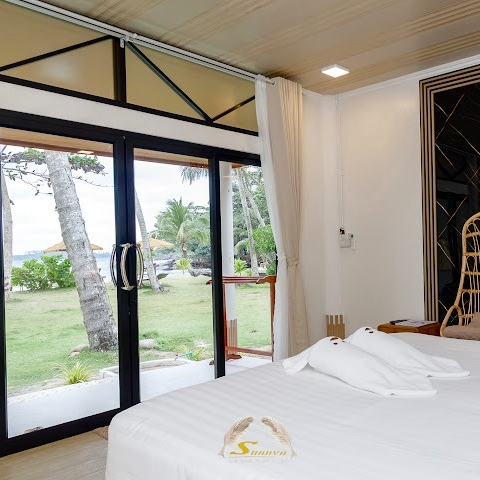 Bedroom with sliding glass doors overlooking a green yard and water; white bedding and curtains.