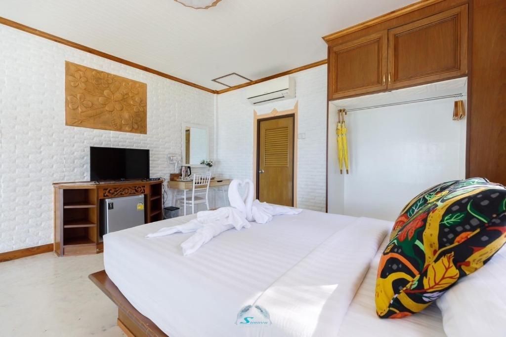 Bedroom with a bed, TV, mini-fridge, desk, wooden cabinets, and white walls.