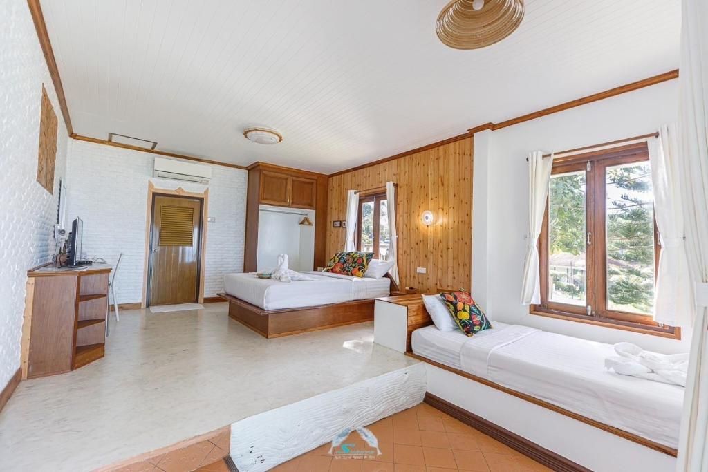 Spacious hotel room with bed, window seat, and wood-paneled wall. White and tan tones with natural light.
