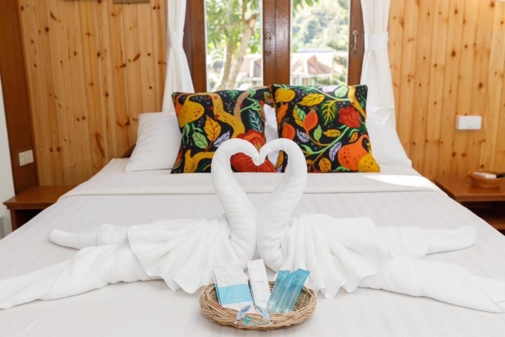 Bedroom with wooden paneling, white linens, swan towel art, and colorful pillows. Basket of toiletries.